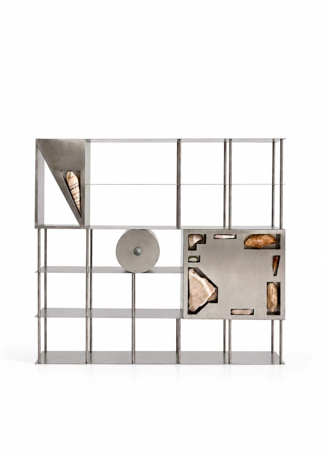 A wide steel shelving unit of open bays, a large spiral shell held in a triangular corner panel at the top left, a circular steel disc at the centre, and a right-hand panel inset with rock and shell in cut windows