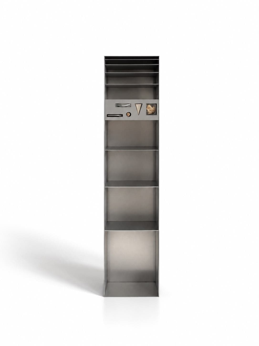 A tall narrow column of brushed steel standing alone: a stack of thin close-set trays at the top, four open bays below, and across the upper third a panel inset with a slot, a pale triangular wedge, a small copper bead and a piece of rock framed in a lit window